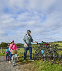 A scenic photo of Waterford Greenway in County Waterford, featuring a paved path, lush greenery, and distant hills under a clear blue sky.