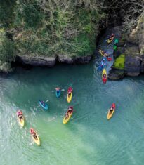 Two people kayaking in calm waters near rocky cliffs under a blue sky at Ladies Cove, Dunmore Adventure Co, Waterford.